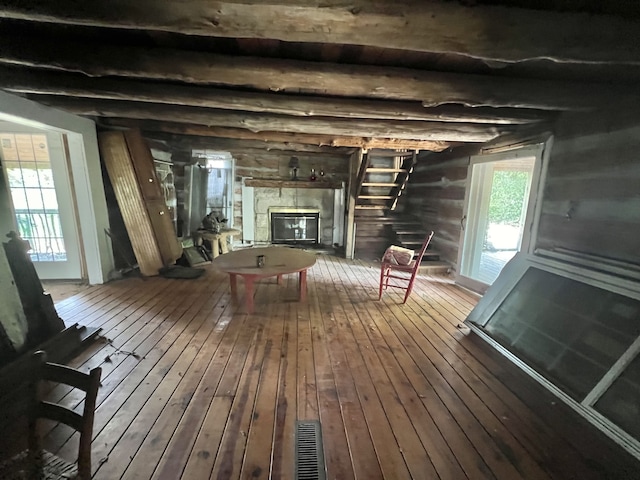 interior space with wooden walls, beam ceiling, hardwood / wood-style floors, and a stone fireplace