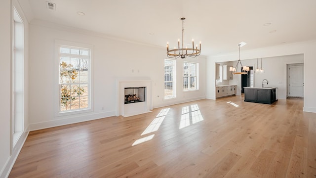 unfurnished living room with ornamental molding, sink, a notable chandelier, and light hardwood / wood-style floors