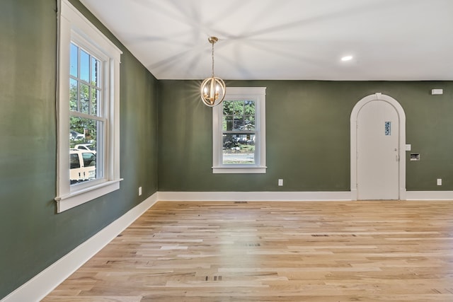 spare room with a chandelier, light hardwood / wood-style flooring, and a healthy amount of sunlight