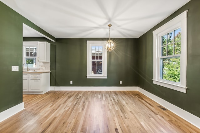 unfurnished dining area with a chandelier, sink, and light wood-type flooring