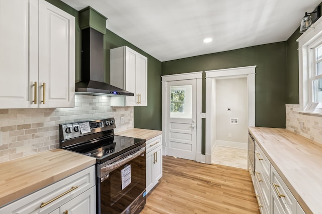 kitchen featuring wall chimney exhaust hood, white cabinets, black range with electric stovetop, and a wealth of natural light