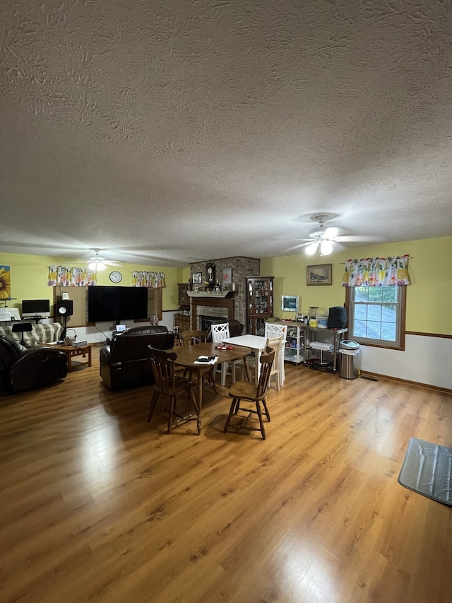 dining space featuring a textured ceiling, ceiling fan, a large fireplace, and wood-type flooring