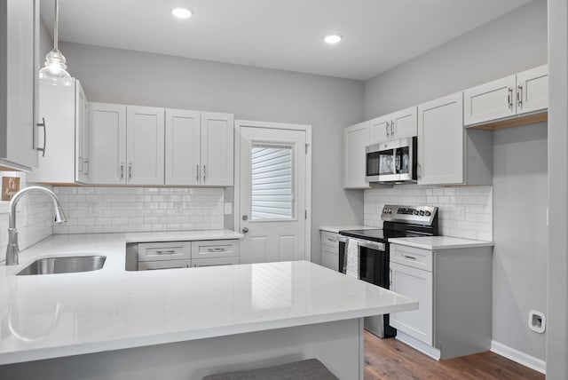 kitchen with dark wood finished floors, a peninsula, a sink, stainless steel appliances, and backsplash