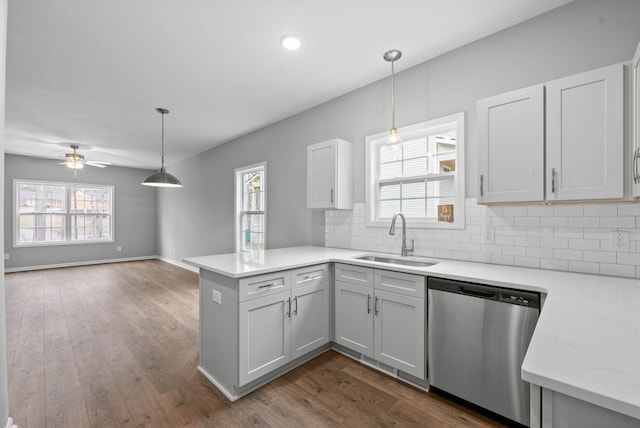 kitchen with backsplash, dishwasher, light countertops, a peninsula, and a sink