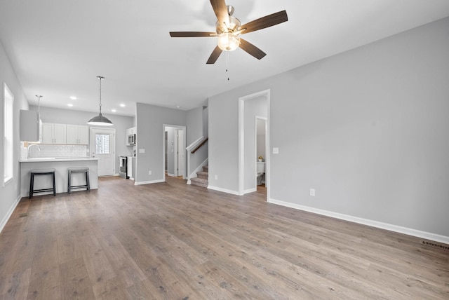 unfurnished living room with wood finished floors, recessed lighting, stairway, baseboards, and ceiling fan