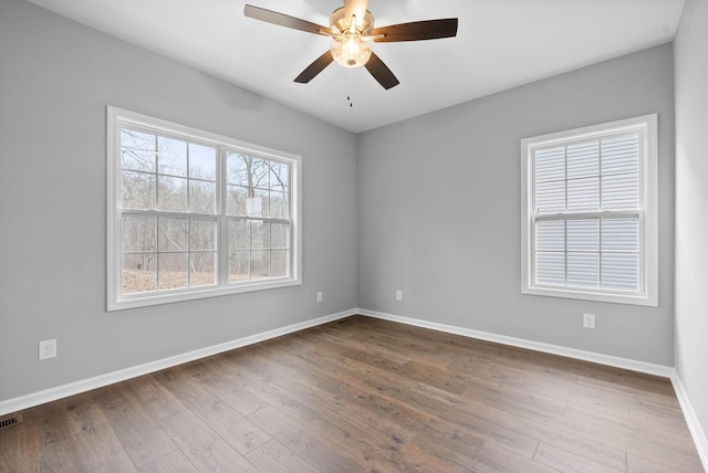 empty room with dark wood-style floors, visible vents, a ceiling fan, and baseboards