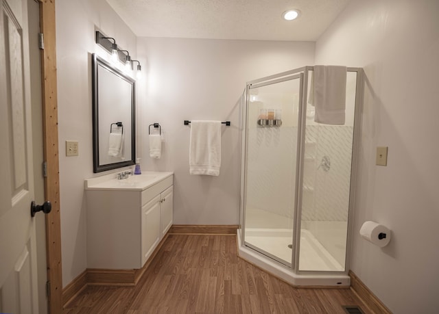 bathroom with a textured ceiling, wood finished floors, vanity, baseboards, and a stall shower