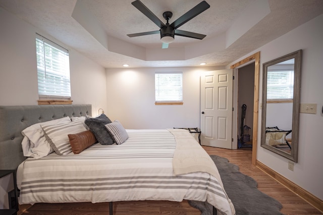 bedroom featuring a textured ceiling, baseboards, a raised ceiling, and wood finished floors