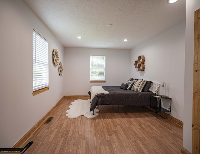 bedroom with light wood finished floors, recessed lighting, visible vents, a textured ceiling, and baseboards