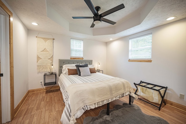 bedroom featuring baseboards, multiple windows, light wood-style flooring, and a textured ceiling