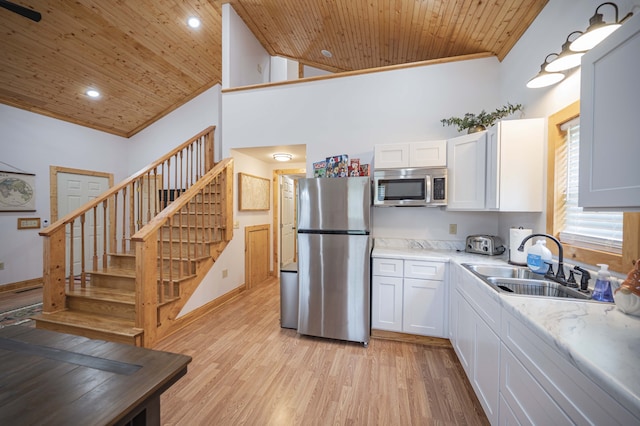 kitchen with stainless steel appliances, a sink, wood ceiling, white cabinetry, and ornamental molding