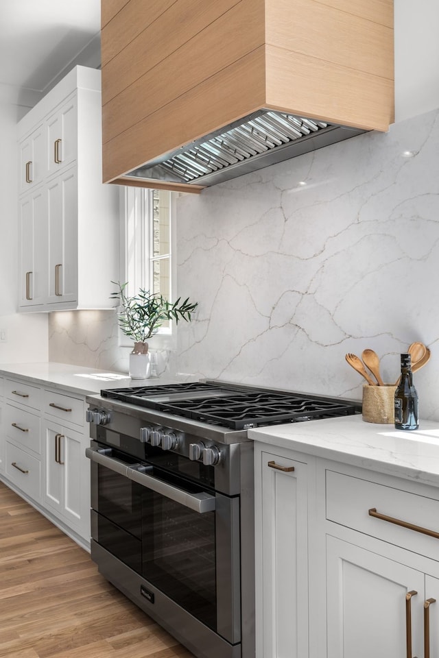 kitchen featuring white cabinets, stainless steel range with gas cooktop, light wood-type flooring, and premium range hood