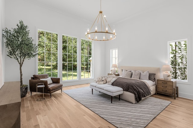 bedroom with a notable chandelier, crown molding, a towering ceiling, and light hardwood / wood-style flooring