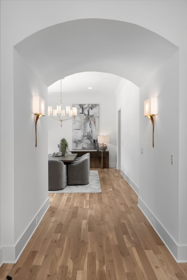 hallway with light hardwood / wood-style floors, a chandelier, and vaulted ceiling