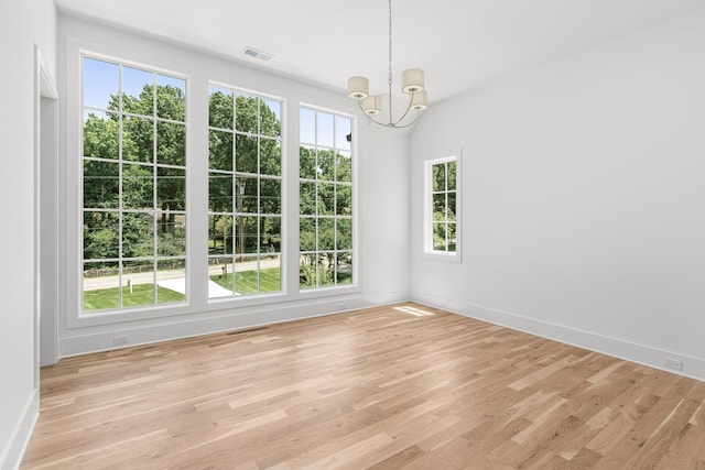 unfurnished room with a healthy amount of sunlight, light wood-type flooring, and a chandelier