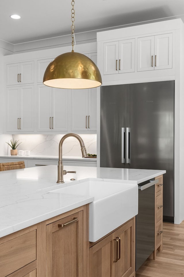 kitchen with light wood-type flooring, light stone counters, backsplash, hanging light fixtures, and white cabinetry