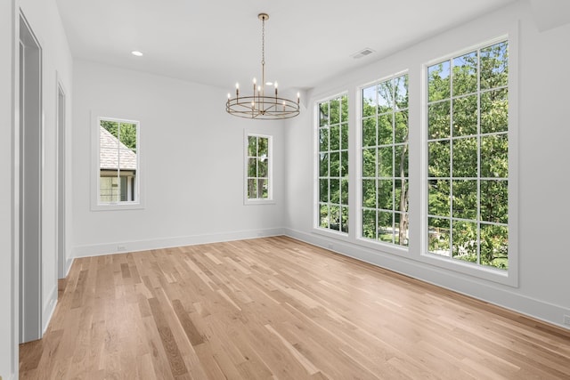 spare room with a healthy amount of sunlight, a notable chandelier, and light wood-type flooring