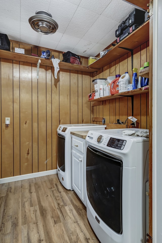 clothes washing area with washing machine and clothes dryer, light hardwood / wood-style flooring, wood walls, and cabinets