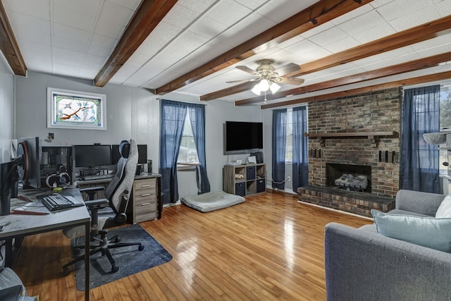 office area featuring a brick fireplace, ceiling fan, beamed ceiling, and hardwood / wood-style flooring