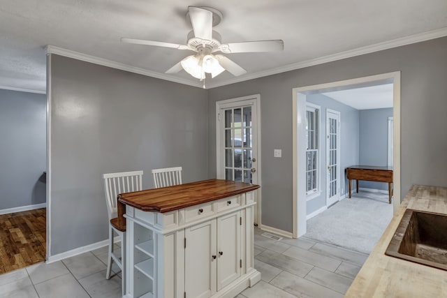 kitchen with white cabinetry, ornamental molding, ceiling fan, and light tile flooring