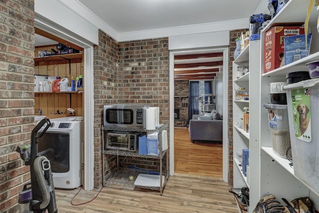 interior space featuring brick wall, washer and clothes dryer, stainless steel microwave, and light hardwood / wood-style floors