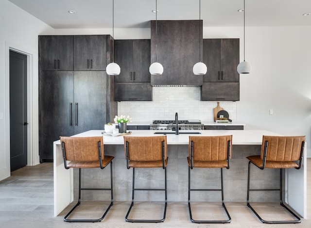 kitchen with hanging light fixtures, light hardwood / wood-style flooring, dark brown cabinetry, sink, and tasteful backsplash