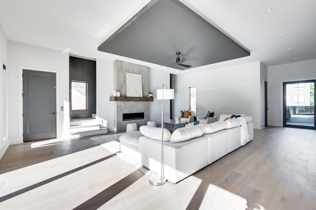 living room with a tile fireplace, light wood-type flooring, and ceiling fan