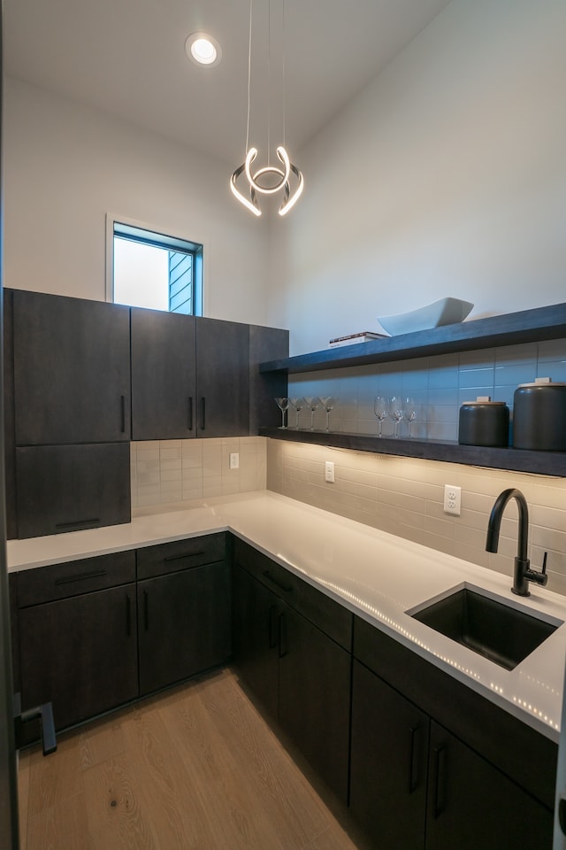 kitchen with a chandelier, tasteful backsplash, light wood-type flooring, sink, and pendant lighting