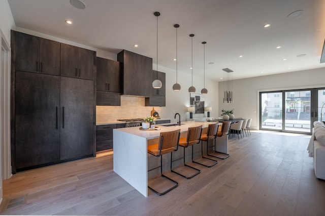 kitchen featuring decorative light fixtures, light hardwood / wood-style flooring, backsplash, a breakfast bar area, and an island with sink