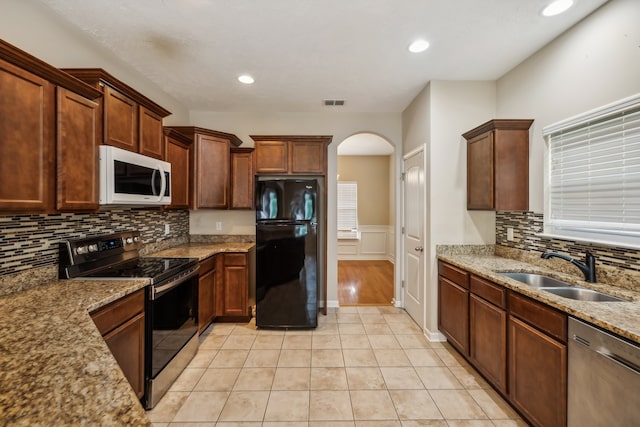 kitchen featuring tasteful backsplash, sink, light stone countertops, appliances with stainless steel finishes, and light tile patterned floors