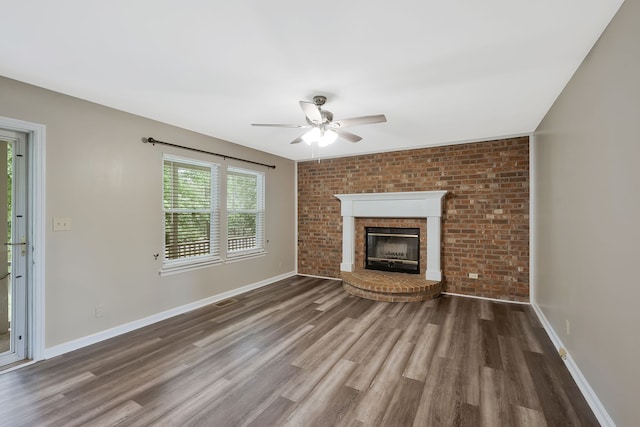 unfurnished living room with dark hardwood / wood-style floors, ceiling fan, brick wall, and a brick fireplace