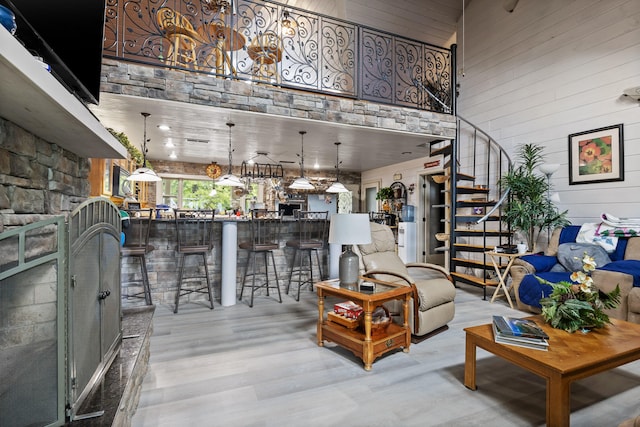 living room with wooden walls, indoor bar, a towering ceiling, stairway, and light wood-style floors