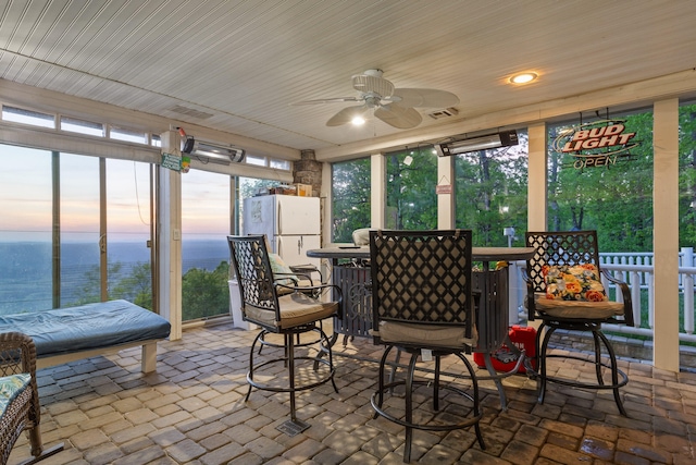 sunroom featuring a ceiling fan, a water view, visible vents, and a dry bar