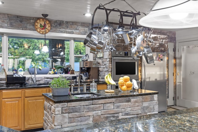 kitchen featuring dark stone counters, stainless steel appliances, a sink, and decorative light fixtures