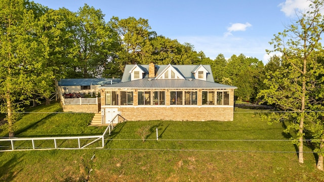 back of house featuring a sunroom, metal roof, a chimney, and a lawn