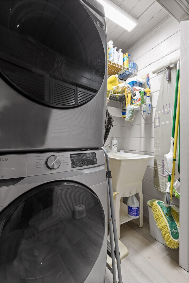 washroom with stacked washer / drying machine, laundry area, and light wood-style flooring