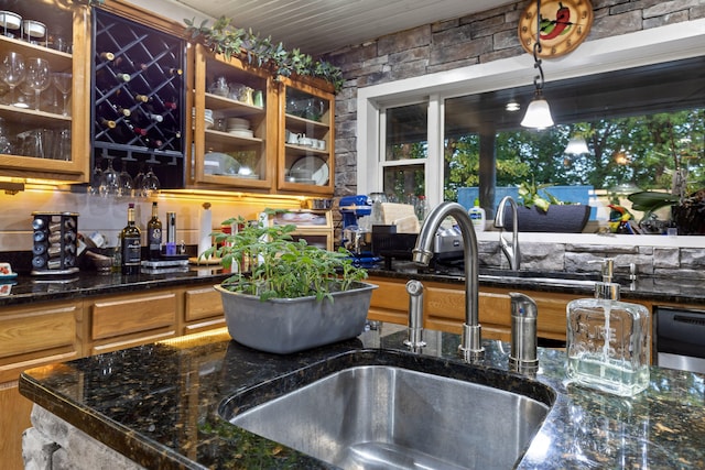 kitchen with dishwashing machine, a sink, hanging light fixtures, dark stone countertops, and glass insert cabinets