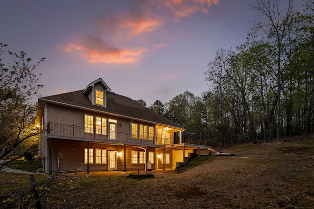 back house at dusk featuring a balcony, a yard, and a patio