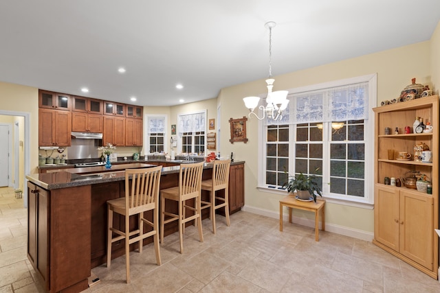 kitchen featuring a notable chandelier, dark stone countertops, a healthy amount of sunlight, and pendant lighting