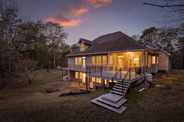 back house at dusk featuring a wooden deck, a yard, and a patio area