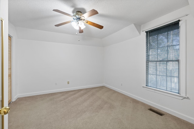 carpeted empty room with a textured ceiling, a healthy amount of sunlight, and ceiling fan