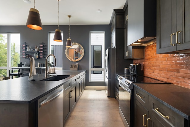 kitchen featuring appliances with stainless steel finishes, a center island with sink, sink, light hardwood / wood-style floors, and wall chimney exhaust hood