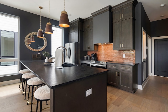 kitchen featuring wall chimney range hood, light wood-type flooring, and an island with sink