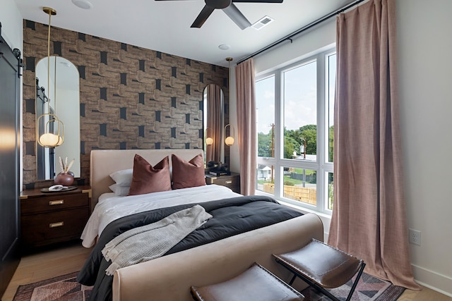 bedroom featuring light wood-type flooring, a barn door, and ceiling fan