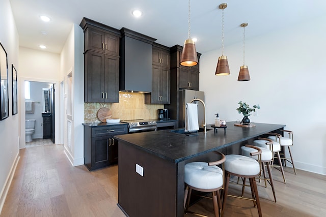 kitchen featuring dark brown cabinetry, light hardwood / wood-style floors, backsplash, an island with sink, and stainless steel appliances