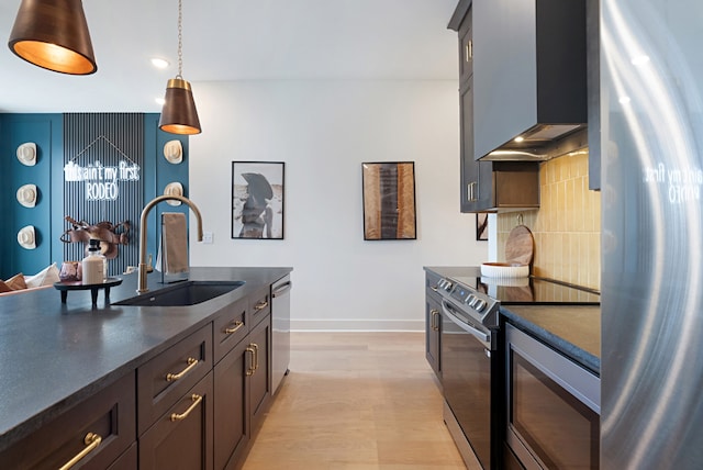 kitchen with appliances with stainless steel finishes, backsplash, light hardwood / wood-style flooring, sink, and wall chimney range hood