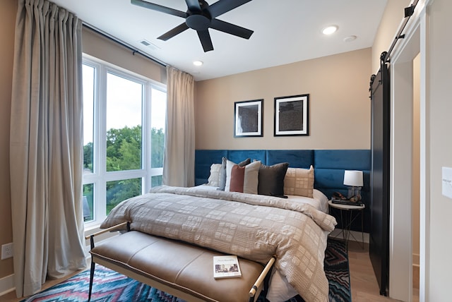 bedroom featuring a barn door, hardwood / wood-style floors, and ceiling fan