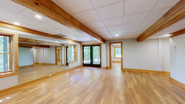 empty room with beamed ceiling, light hardwood / wood-style flooring, and a drop ceiling