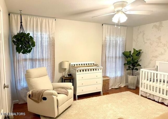 bedroom with ceiling fan, a nursery area, and hardwood / wood-style flooring