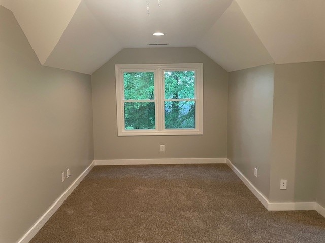 additional living space featuring dark carpet and vaulted ceiling